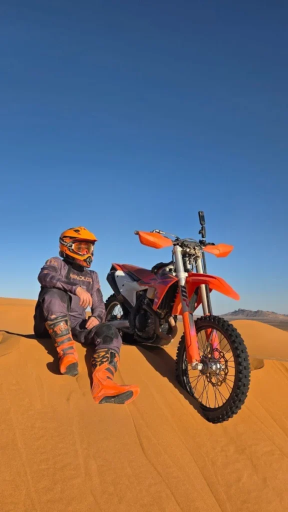 Rider resting beside his KTM enduro motorcycle on a Sahara dune