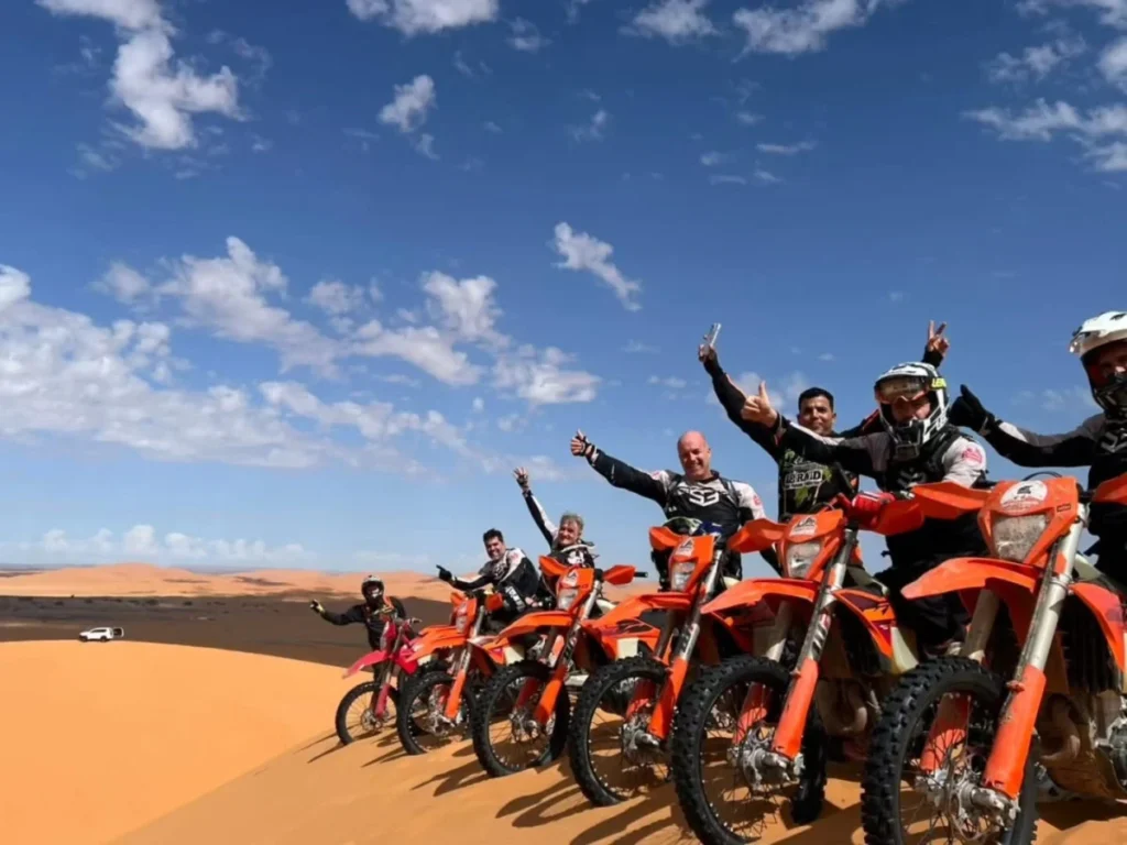Happy riders on KTM enduro bikes on a dune in the Merzouga Sahara
